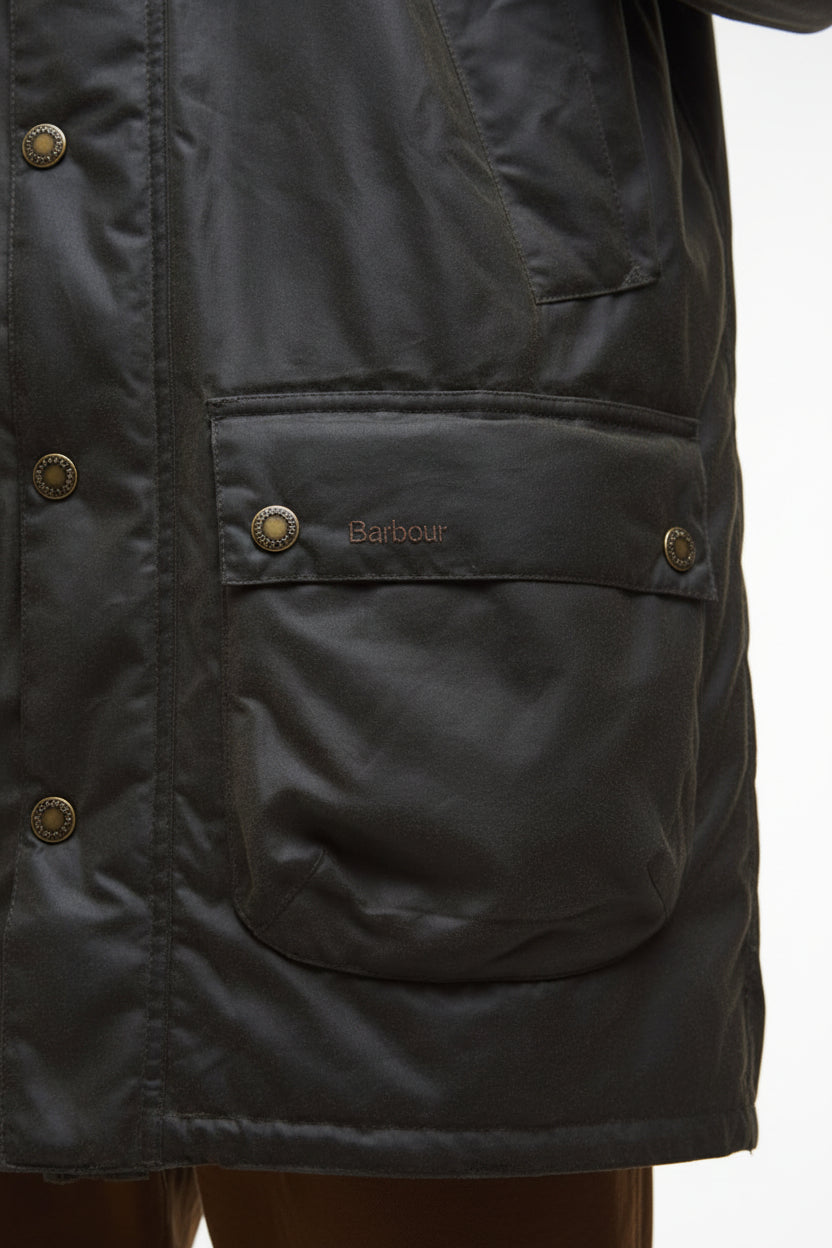 Dark olive wax parka front pocket with Barbour label and buttoned flap.