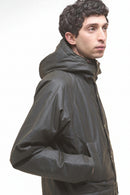 Dark olive wax parka jacket in side profile, hood up and long sleeves.