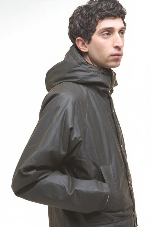 Dark olive wax parka jacket in side profile, hood up and long sleeves.