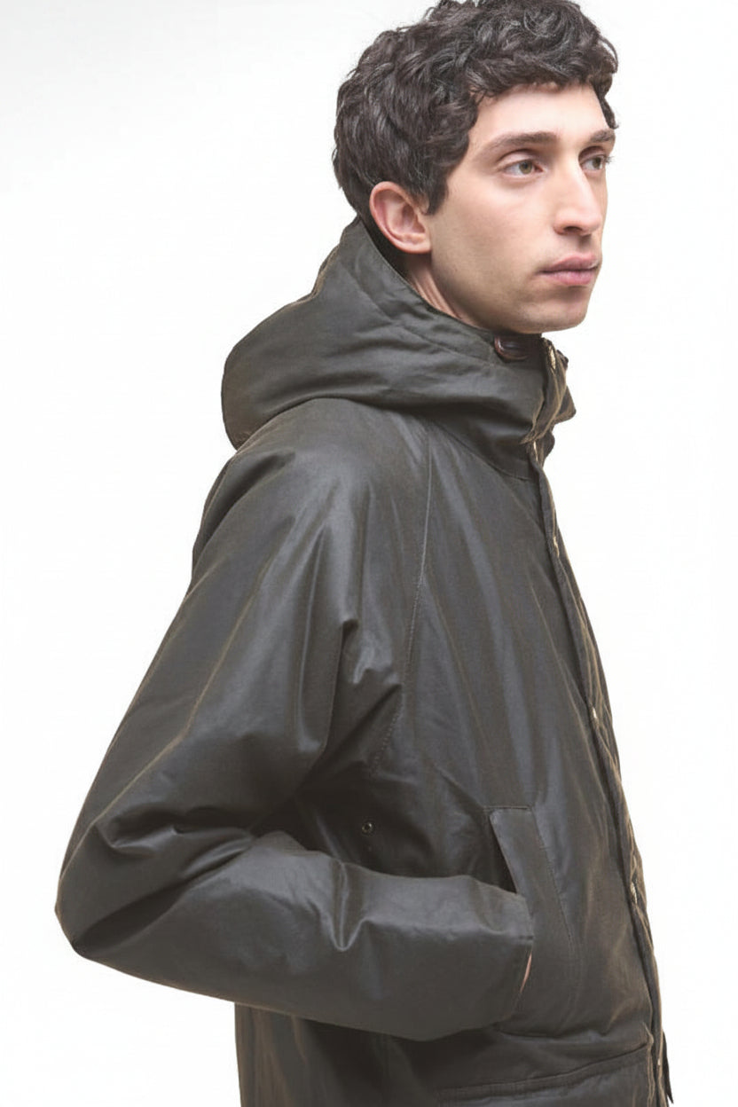 Dark olive wax parka jacket in side profile, hood up and long sleeves.