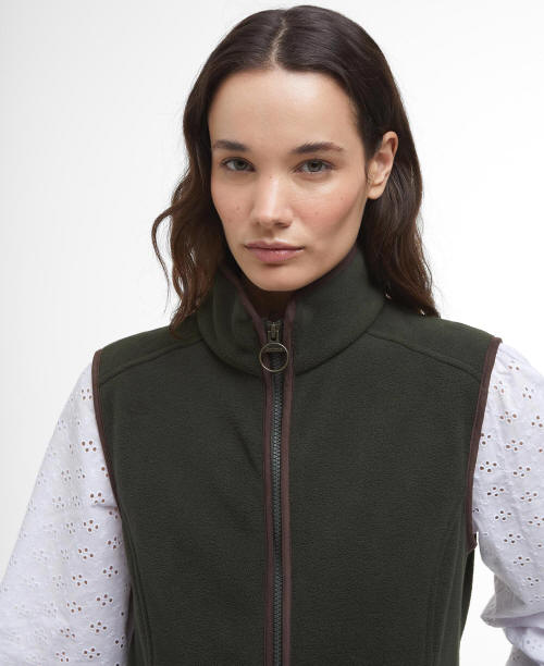 Sage green fleece gilet with high collar and central zip, worn over patterned sleeves.