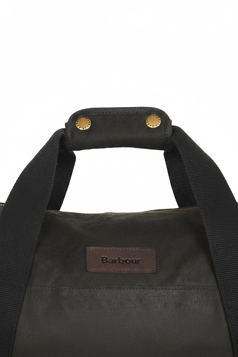Dark olive duffle bag close-up: webbing handles and Barbour logo patch on front