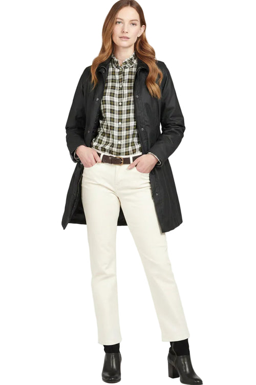 Barbour black waxed waterproof coat over plaid top and cream trousers