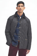 Men's black quilted jacket worn with blue plaid shirt, Barbour logo on chest