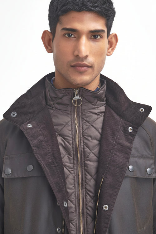 Men's Barbour wax jacket in dark brown with stand collar, snap buttons, and grommet cord.