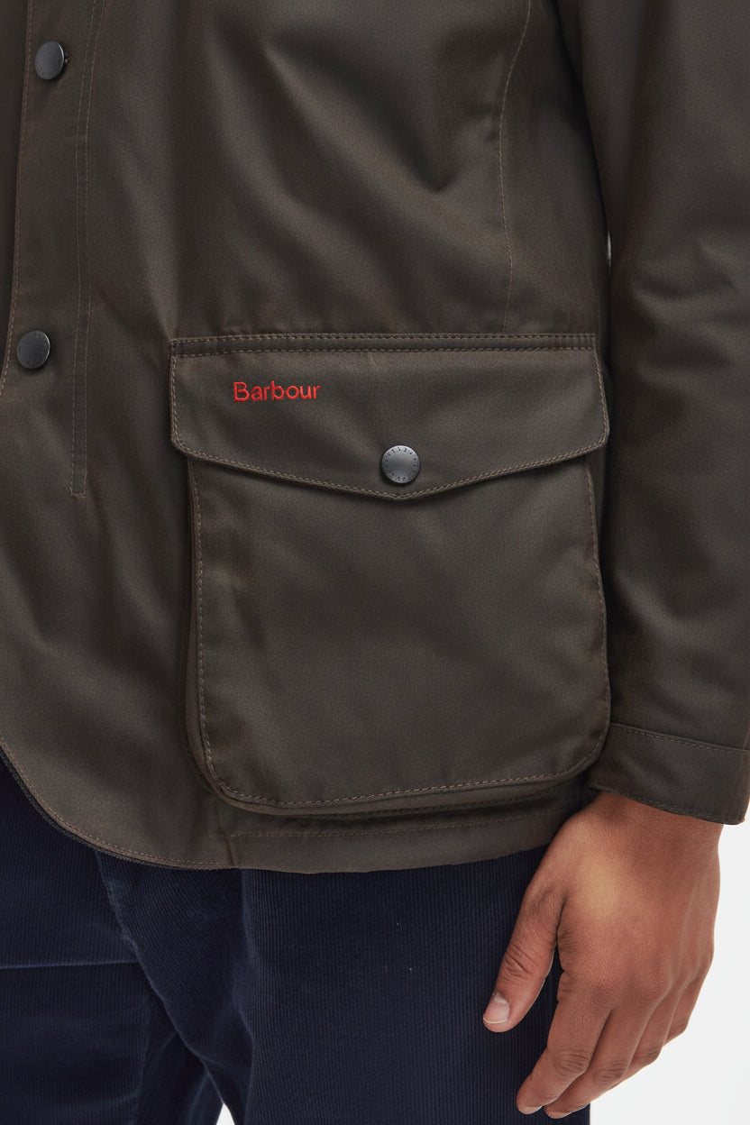 Men's Barbour wax jacket pocket detail in dark brown with snap flap and button.