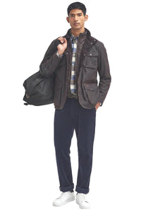 Men's Barbour wax jacket in dark brown worn with dark pants and visible flap pockets.