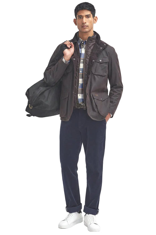 Men's Barbour wax jacket in dark brown worn with dark pants and visible flap pockets.