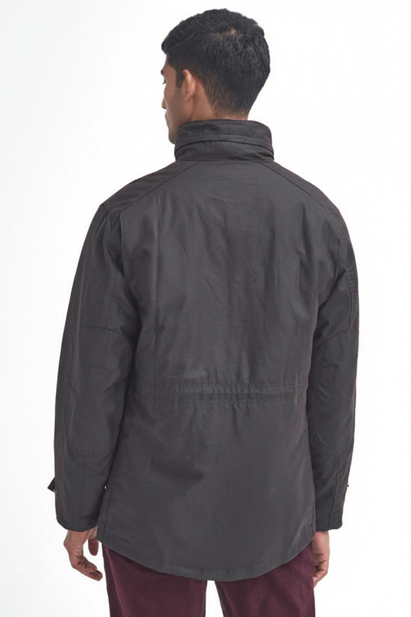 A man viewed from the back wearing a barbour sapper wax rustic jacket with a high collar and a drawstring waist, paired with burgundy pants, against a plain white background.