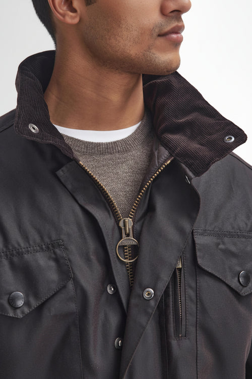 Close-up of a man wearing Barbour-Mens-Wax-Sapper-Jacket-Rustic-MWX0020RU93 waxed cotton jacket with a corduroy collar, layered over a gray knit sweater and white t-shirt.