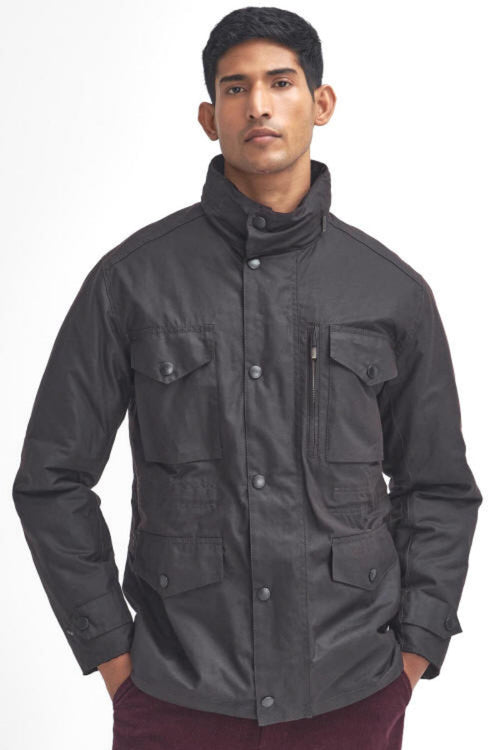 A man wearing a barbour sapper wax rustic jacket with a high stand-up collar and multiple front pockets, paired with burgundy corduroy pants, against a plain white background.