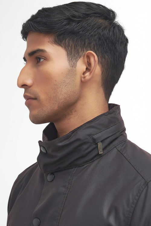Close-up side profile of a man wearing a barbour sapper wax rustic  high-collar jacket against a plain white background.