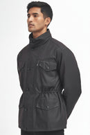 A man wearing a barbour sapper rustic jacket with a high collar, button front, and multiple flap pockets, photographed against a plain white studio background.