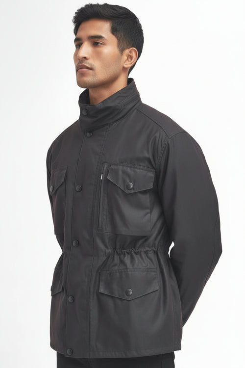 A man wearing a barbour sapper rustic jacket with a high collar, button front, and multiple flap pockets, photographed against a plain white studio background.