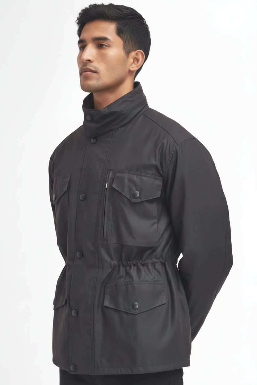 A man wearing a barbour sapper rustic jacket with a high collar, button front, and multiple flap pockets, photographed against a plain white studio background.