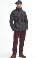 A man modeling a barbour sapper wax rustic jacket with a high collar, paired with burgundy corduroy trousers and brown boots, against a plain white background.