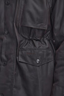 Close-up of a dark charcoal gray waxed cotton jacket, showing a buttoned chest pocket with the Barbour logo embroidered on it.