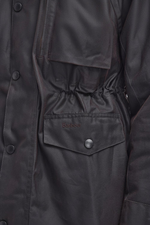 Close-up of a dark charcoal gray waxed cotton jacket, showing a buttoned chest pocket with the Barbour logo embroidered on it.