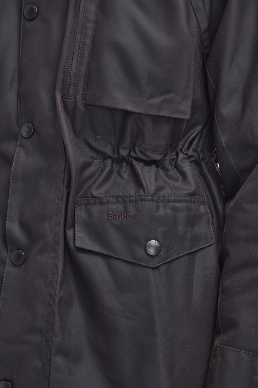 Close-up of a dark charcoal gray waxed cotton jacket, showing a buttoned chest pocket with the Barbour logo embroidered on it.