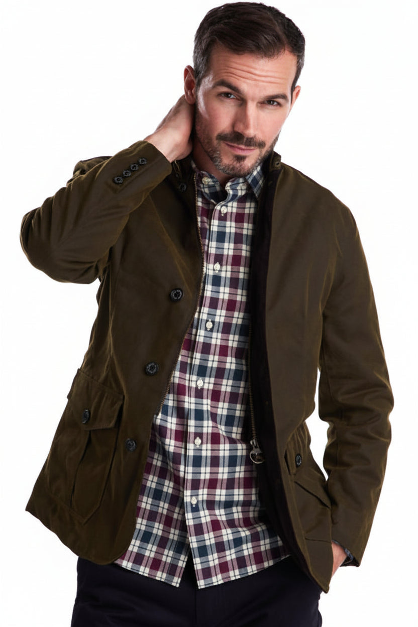 Men's olive wax jacket worn open over plaid shirt; flap pockets and button cuffs.