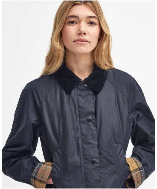 Navy wax jacket with cord collar, button placket, and plaid cuffs showing at wrists