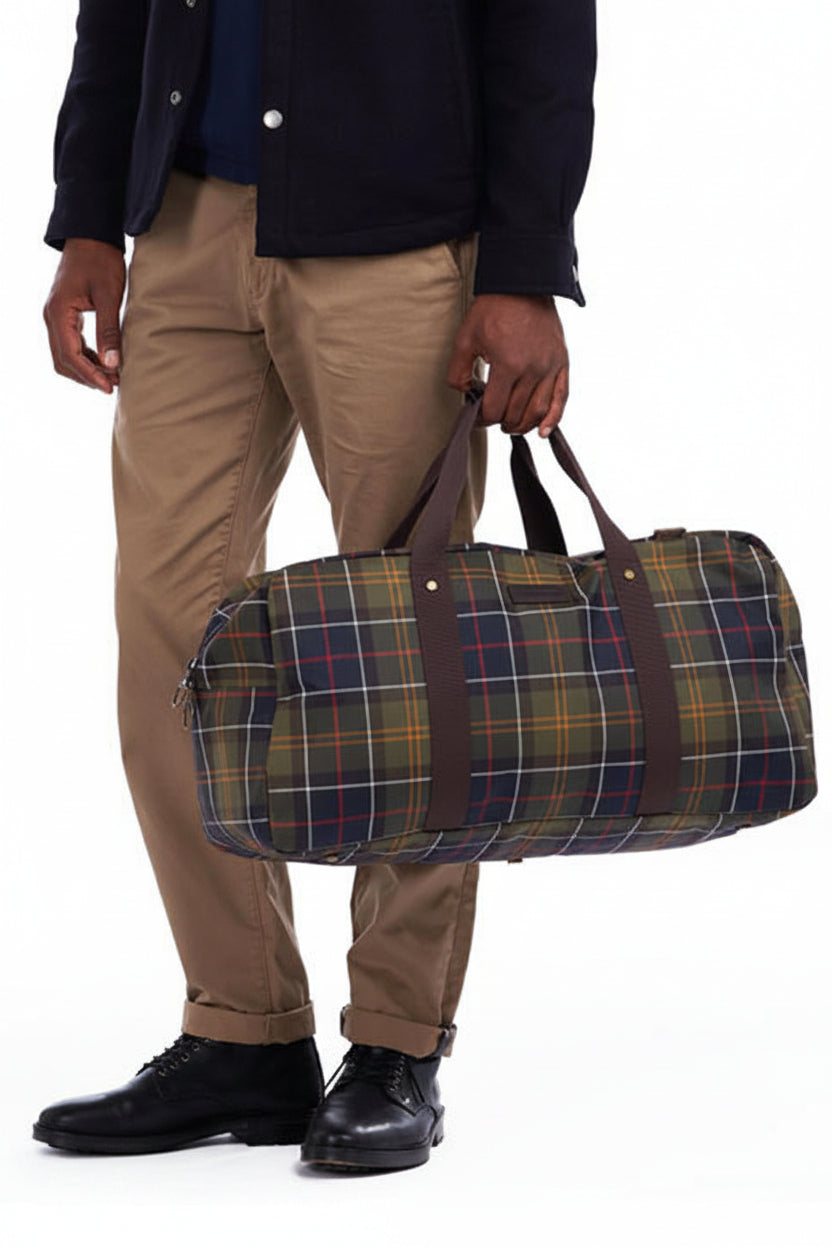 Plaid tartan holdall bag being carried; wide shoulder strap and buttoned end tabs