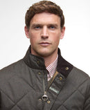 Dark olive quilted jacket close-up with zip front, gold buttons, and Barbour logo