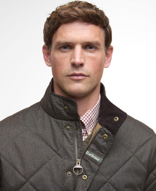 Dark olive quilted jacket close-up with zip front, gold buttons, and Barbour logo