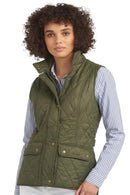 Olive quilted Barbour gilet with button pockets and zip front, worn with striped shirt.