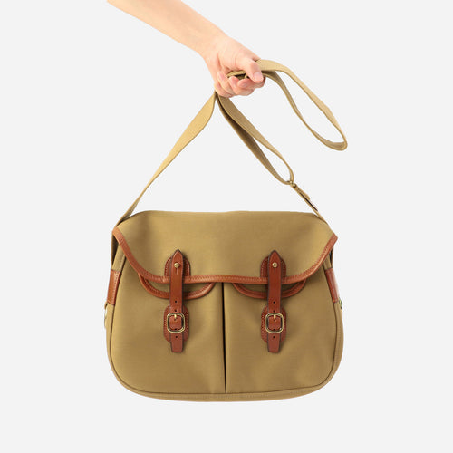 Khaki small crossbody bag held by its strap with brown leather buckle accents