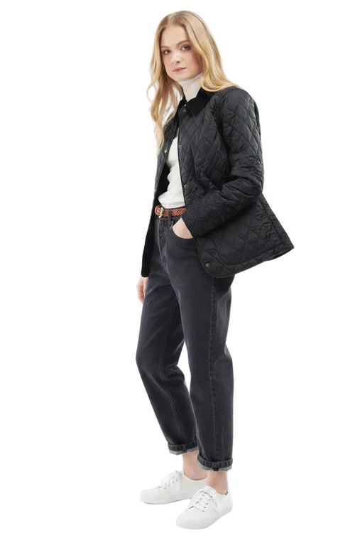 Black quilted women’s jacket with button front, side profile view with jeans styling