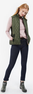 Olive quilted gilet worn over dark jeans, standing collar, and full-length zip